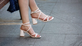 Female legs in summer shoes on high heels, woman in white sandals sitting on city street